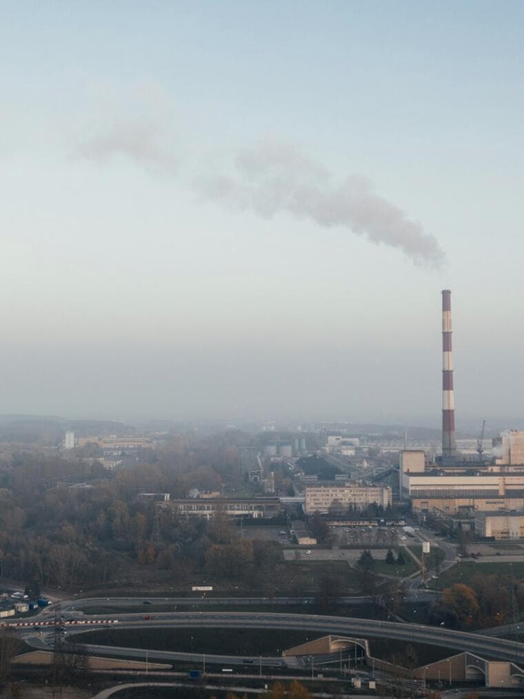 An industrial stack rising through low haze over a valley.